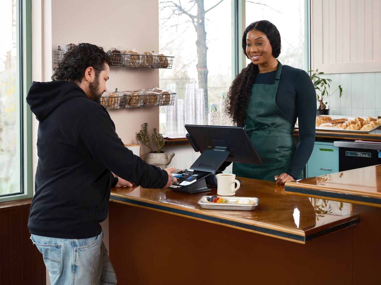 A customer uses a contactless payment system at a café counter, served by a friendly barista.