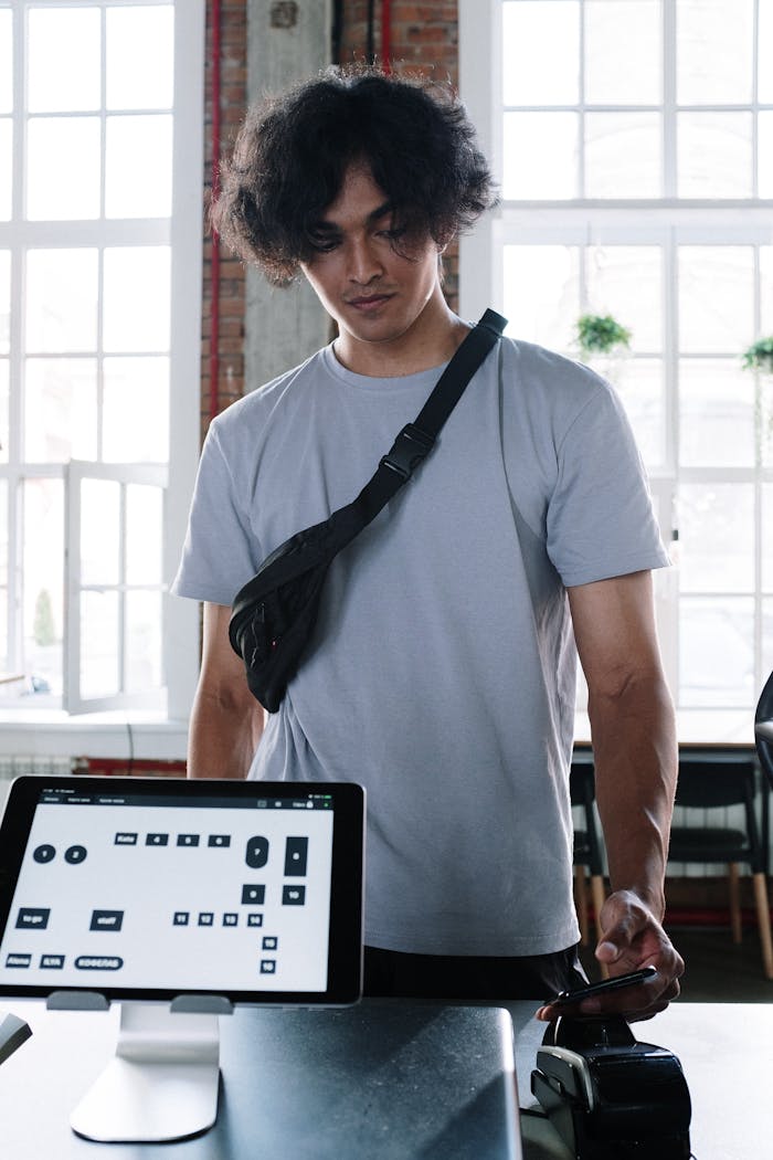 A stylish young man makes a contactless payment using a smartphone in a modern café setting.