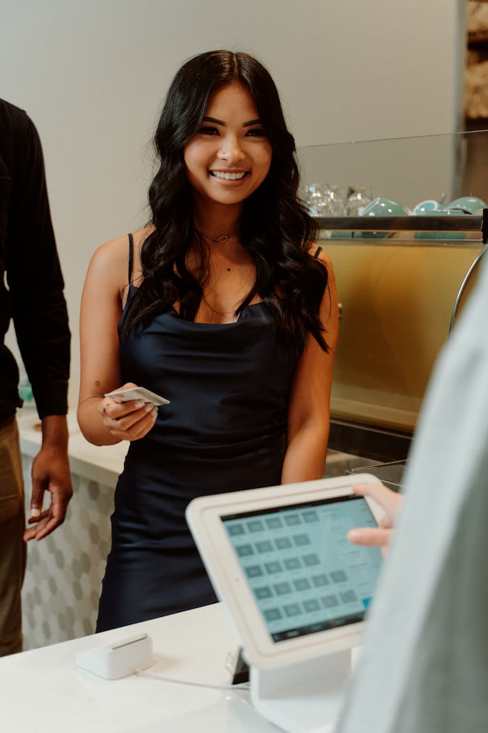 A woman in a black dress smiling while making a cashless payment at a store.