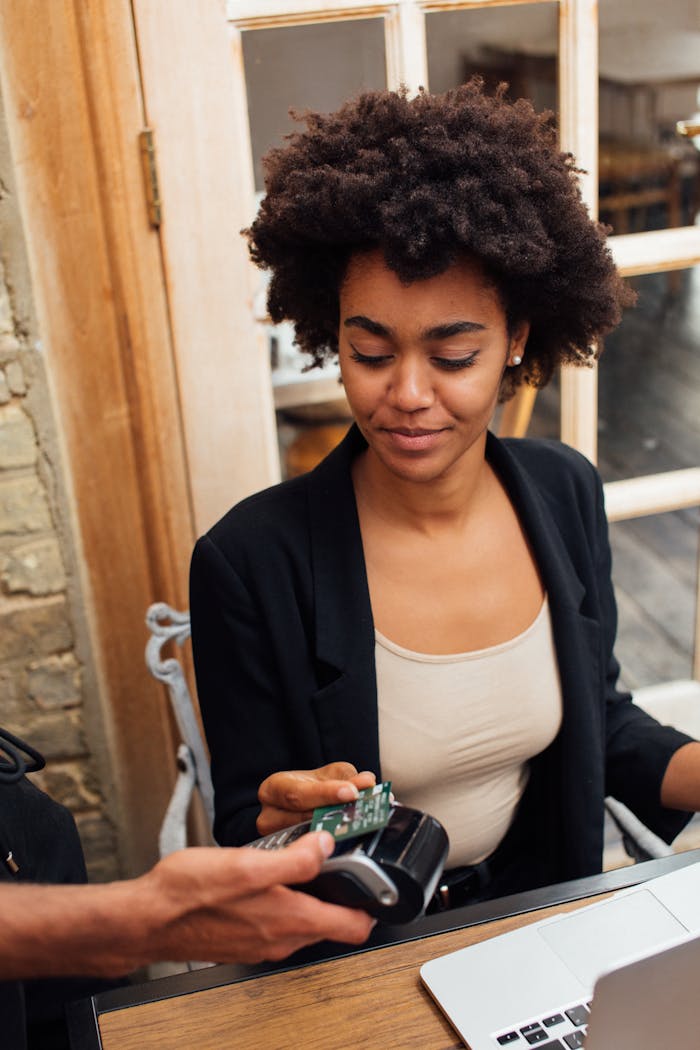 Young woman uses contactless payment in a cozy café setting, with a focus on technology and ease.
