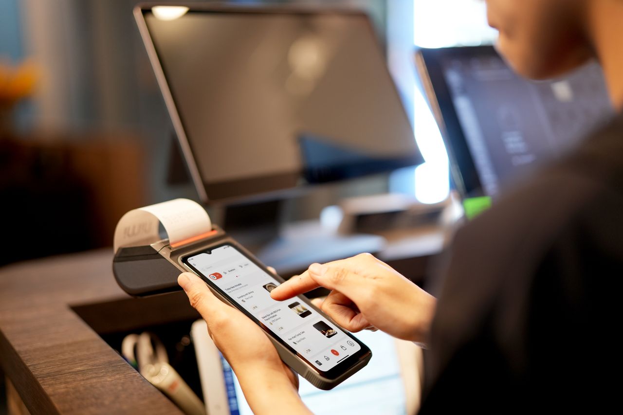 services-03 A person using a smartphone for payment at a modern POS terminal indoors.