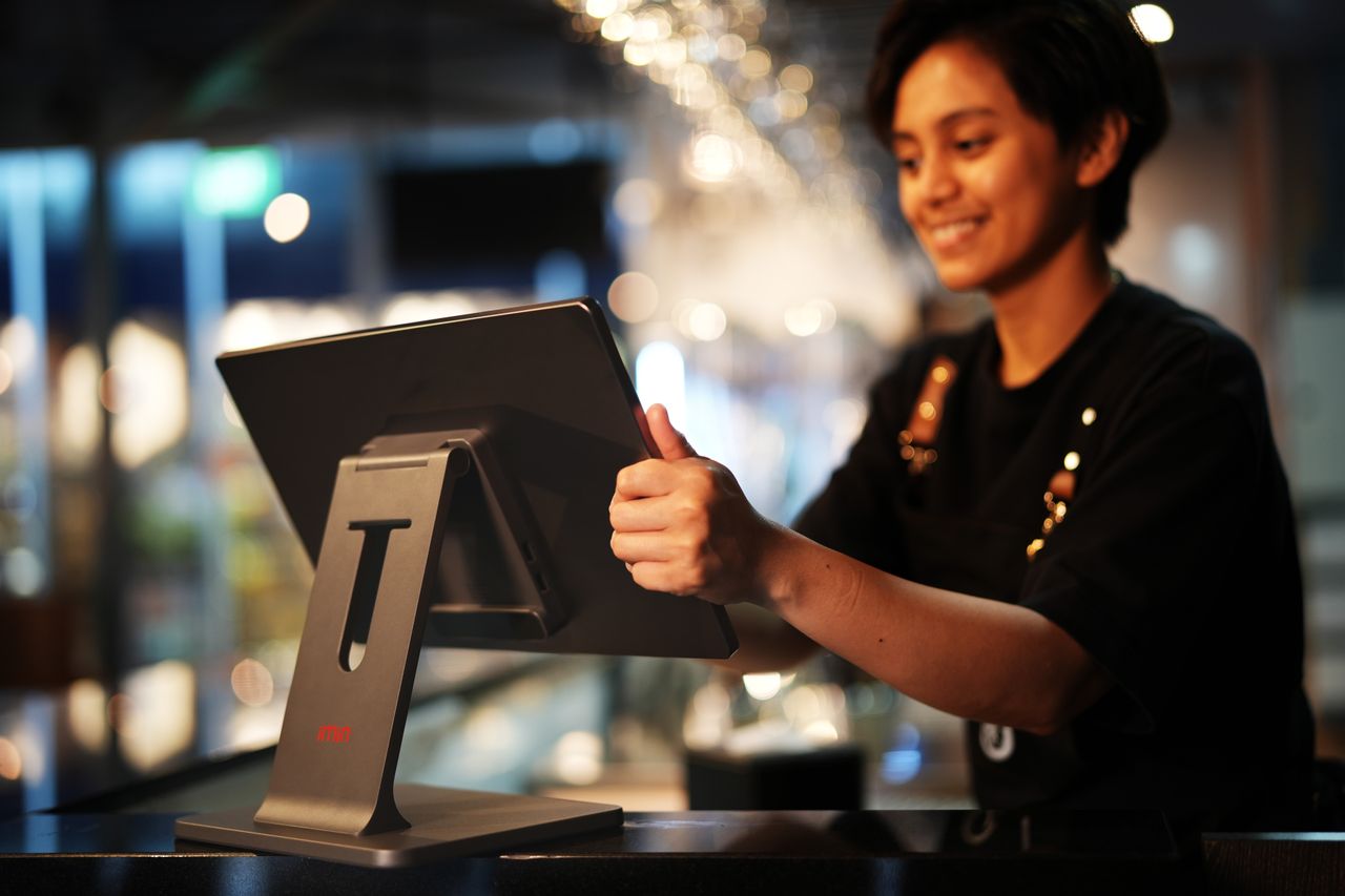 hero-img-02 Smiling female cashier using a touchscreen in a modern restaurant setting.