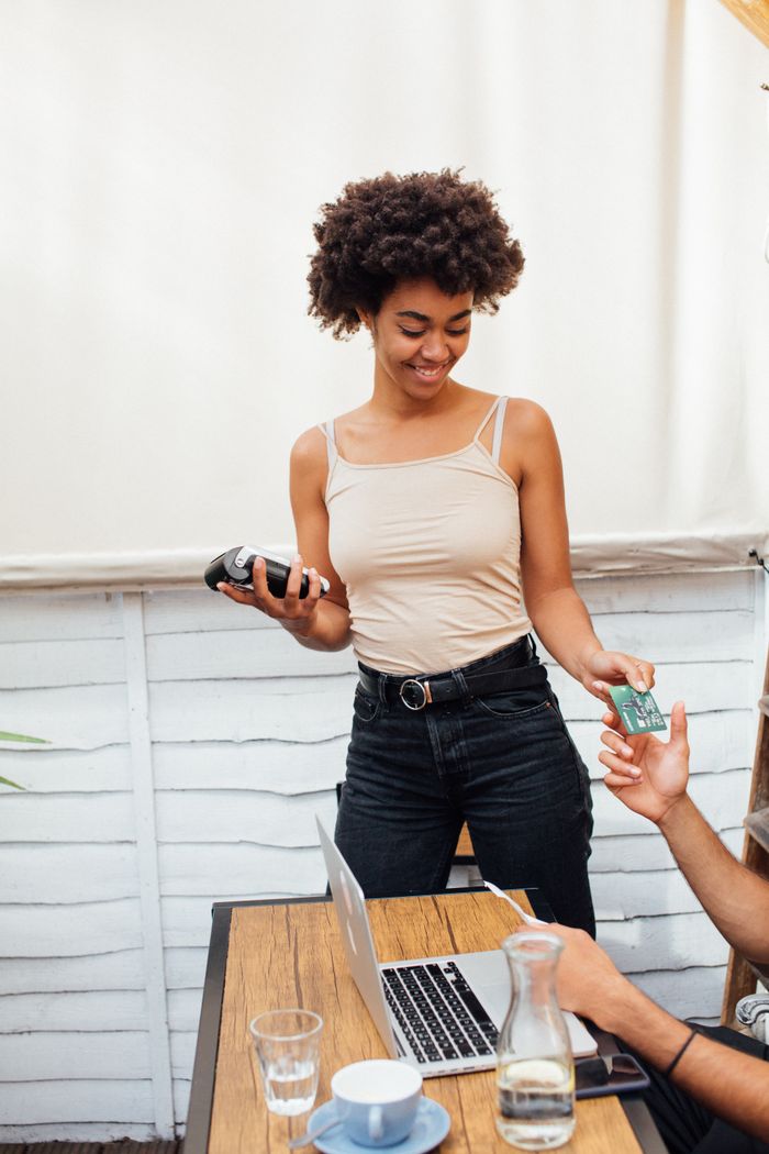 why-choose-us Woman smiling while handling payment transaction in a café setting.