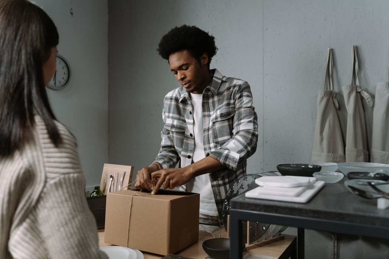 gallery-6 A man carefully packs a box in a retail setting, preparing goods for a customer.